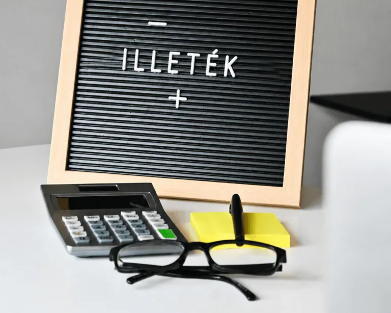 számológép, szemüveg és "illeték" felirat egy táblán