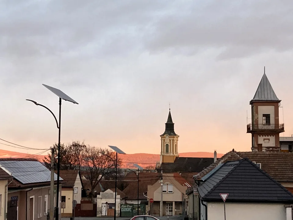 Naplemente Sátoraljaújhely belvárosában, templomtoronnyal és napenergiát hasznosító utcai lámpákkal a háttérben